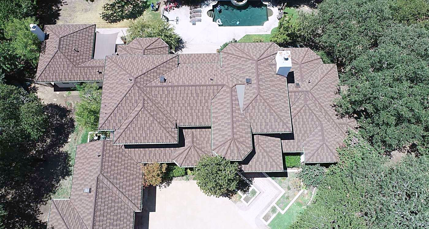 A large brick home from above with a new brown architectural shingle roof